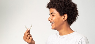 teenage boy holding a clear aligner and smiling