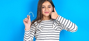 teen with a thumbs up holding a clear aligner