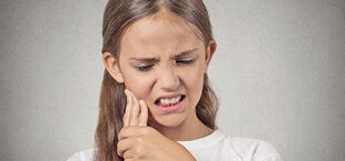 girl holding her face with tooth pain